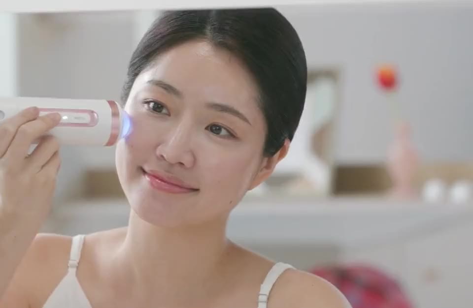 A woman holds the device to her cheek, its plasma head lit blue