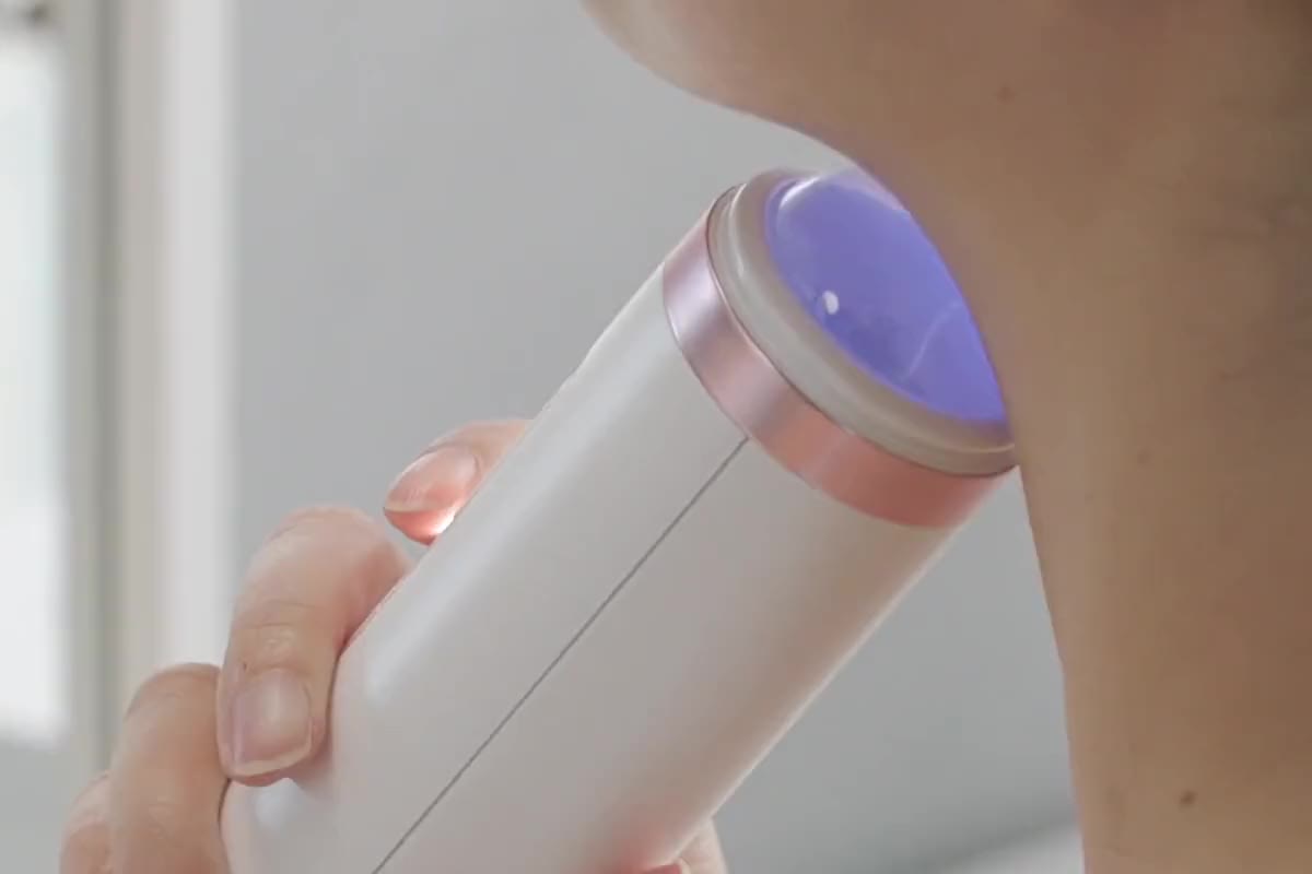 The plasma head, lit violet, glides under a woman's jaw